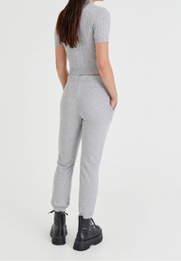 Grauer, verkürzter Kabelstrickpullover mit kurzen Ärmeln, kombiniert mit grauen, schmal zulaufenden Jogginghosen mit Seitentaschen und elastischen Bündchen, getragen mit schwarzen Plateaustiefeln.