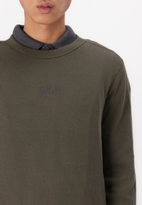 Pulover ribbed de culoare verde măslin, cu guler rotund și guler gri, având un mic logo întunecat „GAP” pe piept.