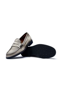 Metallic silver loafers with a stitched toe, decorative strap, and textured rubber sole featuring oval grip patterns. Classic design.