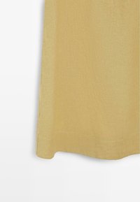 Section inférieure d'une jupe en lin jaune moutarde avec couture visible et ourlet légèrement incurvé sur fond blanc.