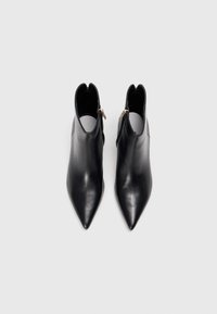 Bottines en cuir noir avec un bout pointu, présentant une fermeture éclair dorée sur le côté et un design découpé au niveau de la cheville. Texture lisse.