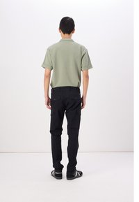 Zielona koszulka polo z krótkim rękawem w połączeniu z czarnymi spodniami cargo z bocznymi kieszeniami. Obuwie to czarne buty z białymi paskami.