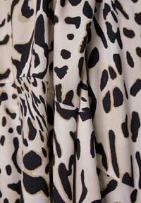Tissu beige avec un motif animal irrégulier noir et marron, plié pour montrer la texture et les détails de la couture.