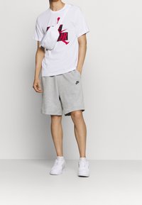 Vit t-shirt med rosa grafik, grå shorts, vita sneakers och en liten vit crossbody-väska. Tillverkad av bomull och syntetiska material, avslappnad design.