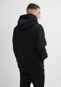 Svart huvtröja med lös passform, långa ärmar och ribbad mudd. Mjuk textur och minimalistisk design, sedd bakifrån.