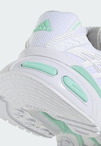 Chaussure de sport Adidas blanche avec des accents vert menthe, semelle rembourrée, tige en mesh respirant et semelle extérieure en caoutchouc texturé pour une meilleure traction.