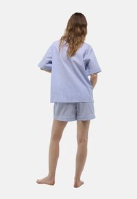 Ensemble de top à manches courtes et short rayé bleu et blanc, présentant une coupe ample, des poignets repliés et une texture en coton doux.