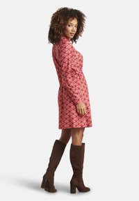 Red patterned dress with long sleeves and a cinched waist, paired with brown knee-high boots. Smooth fabric with a geometric design.