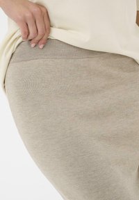 Béžová pletená sukně s elastickým pasem, hladká textura, přiléhavý střih a jemný melírovaný vzor, částečně zakrytá krémovým topem.