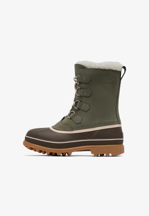 Botte d'hiver haute en vert olive et marron avec laçage devant, semelle en caoutchouc et doublure en polaire blanche visible en haut.