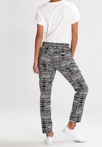 Pantalon à motifs noir et blanc avec une coupe effilée, présentant des motifs géométriques et une texture de tissu lisse, associé à un t-shirt blanc.