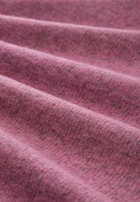 Tissu textile de couleur rose avec une surface douce et texturée présentant de subtiles variations et ondulations, indiquant un poids moyen et une sensation de chaleur.
