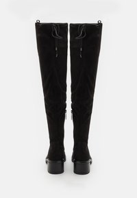 Botas de ante negras por encima de la rodilla con un diseño elegante, que cuentan con cierres de cordones y cremalleras laterales, complementadas por un tacón grueso.