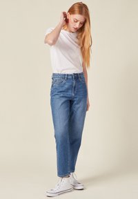 Rechtemodel blauwe denim jeans met een hoge taille, een lichte vervaging en een onafgewerkte zoom, gecombineerd met een fitted wit T-shirt en witte sneakers.