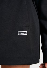 Černá mikina Adidas s texturovanou látkou, malou bílou nášivkou s názvem značky a čistým, jednoduchým designem.