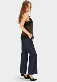 Brązowa satynowa kamizelka z czarną koronką, zestawiona z szerokimi, ciemnoniebieskimi dżinsami i czarnymi szpilkami, o luźnym kroju.