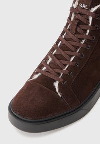 Brune semskede høje sneakers med sort gummisål, med brune snørebånd og hvide tekstil detaljer langs snørehullerne og tungen.