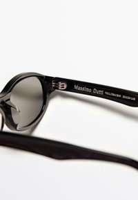 Occhiali da sole neri con design arrotondato e lenti scure. La montatura è in plastica liscia, con un logo argentato sulla stanghetta.