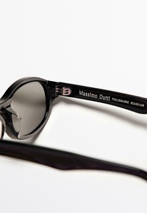 Sorte solbriller med et afrundet design og mørke linser. Stellet er lavet af glat plastik og har et sølvfarvet logo på stangen.