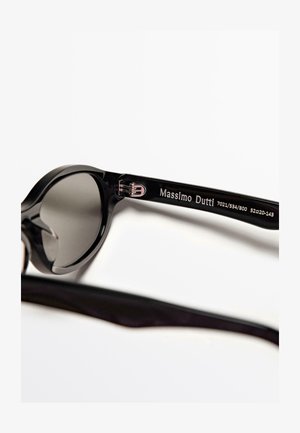 Černé sluneční brýle s kulatým designem a tmavými čočkami. Obruba je vyrobena z hladkého plastu a na stranici je stříbrné logo.