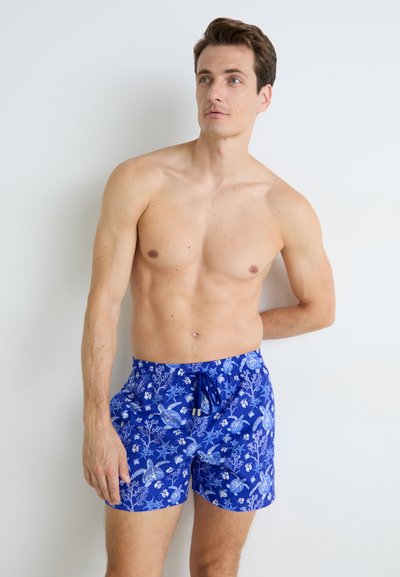 Costume de baie scurt de culoare albastră, cu un cordon la talie, ce prezintă un model vibrant de frunze și flori în nuanțe de albastru deschis și alb pe un fundal închis.