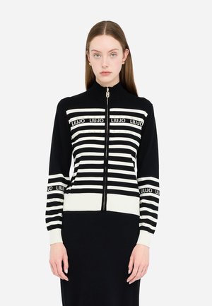 Maglione a zip a righe bianche e nere con colletto alto, caratterizzato da accenti del nome del marchio e dettagli metallici sulle righe. Classica trama a maglia.