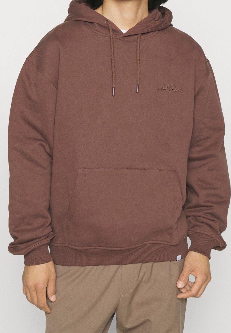 Brauner Kapuzenpullover mit einer Vordertasche, gerippten Bündchen und Saum. Dezentes, gesticktes Logo auf der Brust. Stoff aus Baumwollmischung.