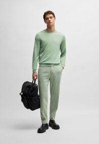 Hellgrüner Pullover, passende Hose und schwarze Tasche. Texturiertes Material, lockere Passform, lange Ärmel, robuste schwarze Stiefel und verstellbare Riemen.
