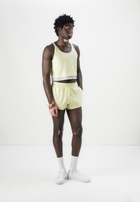 Gul mesh tanktop og shorts sett med hvit elastisk liv, kombinert med hvite joggesko og knelange hvite sokker.
