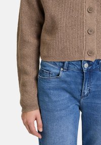 Brun ribbad cardigan med knappstängning, tillsammans med ljusblå jeans med klassisk passform och sidofickor. Mjuk textur, avslappnad design.