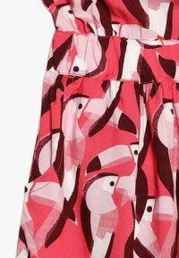 Sukienka z tkaniny bawełnianej z różowym tłem i wyrazistym wzorem tukanów w ciemnoczerwonym i białym kolorze, z gumką w talii dla lepszego dopasowania.