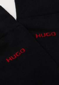 Chaussettes en coton noires avec une texture côtelée et une broderie rouge du logo "HUGO" sur les côtés.