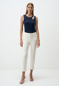 Body senza maniche blu navy con un'apertura a chiave, abbinato a jeans bianchi a vita alta e sandali con tacco argentati. Texture liscia, silhouette aderente.