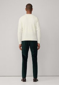 Sudadera de punto blanco con mangas largas, combinada con pantalones de pana verde oscuro y zapatos de cuero marrón, vista desde la parte de atrás.