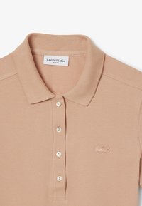 Ljusrosa Lacoste slim fit polo skjorta i texturerad tyg, med tre knappar och Lacoste-logotypen broderad på bröstet.