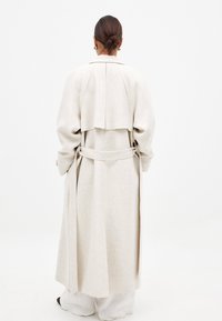 Trench coat de mezcla de lana color beige con un corte relajado, que cuenta con una solapa trasera, cinturón de lazo y mangas largas. Textura suave, diseño de largo hasta el tobillo.