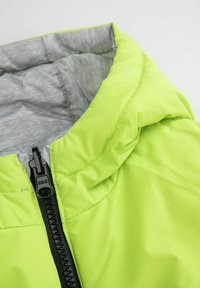 Jasnozielona kurtka z poziomym zamkiem z przodu, teksturowanym materiałem oraz szarym wzorzystym podszewką, z kapturem.