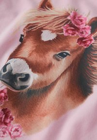 Braunes Pony mit weißen Abzeichen, das einen Blumenkranz trägt, vor einem pinken Hintergrund. Details umfassen feine Fellstruktur und ausdrucksvolle Augen.