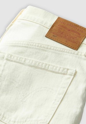 Levi's 501 jeans in cream color with tan leather patch, featuring curved back pocket stitching and a classic denim design.