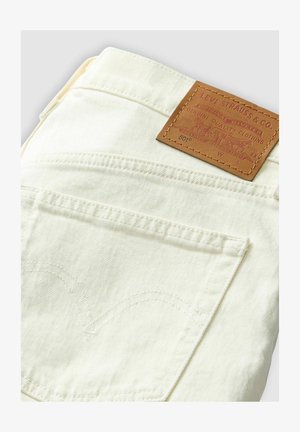 Levi's 501 jeans in cream color with tan leather patch, featuring curved back pocket stitching and a classic denim design.