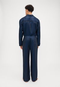 Navy striped pajama set featuring a long-sleeve shirt and wide-leg pants, made from smooth fabric with a relaxed fit and elastic waistband.