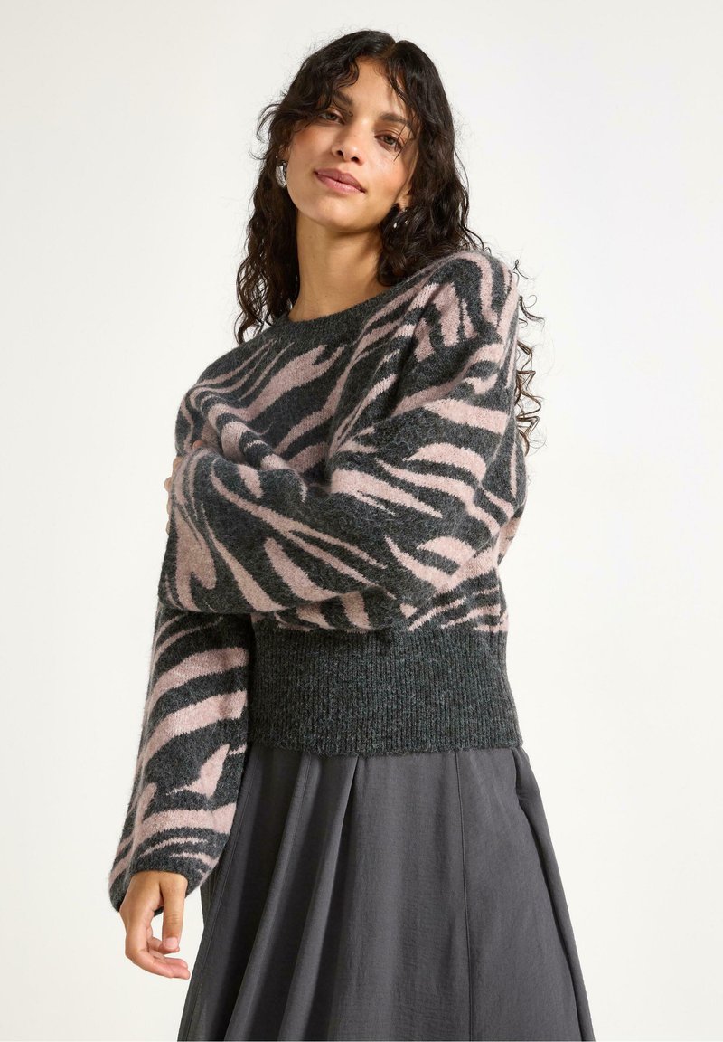 Let svag, strikket sweater med en mørkegrøn bund, prydet med et pink og sort zebra-stribemønster, samt en ribbet kant. Lange ærmer.