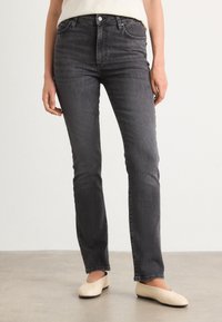 Grijze denim jeans met een aangesloten taille, rechte pijpen en subtiele wassing. Gemaakt met beige platte schoenen op een neutrale achtergrond.
