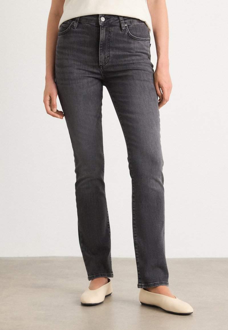 Grijze denim jeans met een aangesloten taille, rechte pijpen en subtiele wassing. Gemaakt met beige platte schoenen op een neutrale achtergrond.