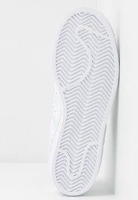 Bílá teniska s texturovanou gumovou podrážkou, hladkým svrškem a třemi modrými pruhy na boku. Obsahuje perforace pro lepší prodyšnost.