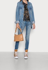 Denimjakke, sort blomsterbluse, blå skinny jeans, brune høj-top sneakers, og en lille tan taske med en rynket hank.