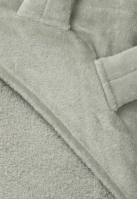 Mjukt grönt fleece-material med en slät yta, visar en plyschtextur och en kontrasterande ribbad kant. Absorberande handduk-liknande material synligt.