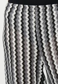 Λεπτομέρεια υφασμάτινου παντελονιού με ανάγλυφη υφή, κατακόρυφες λωρίδες ζιγκ-ζαγκ σε μαύρο, λευκό και γκρι και ελαστική μέση.