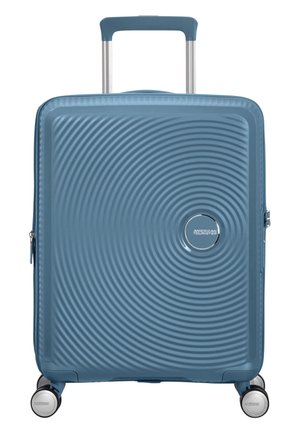 Valigia rigida blu con texture a cerchi concentrici, quattro ruote girevoli e manico telescopico esteso.