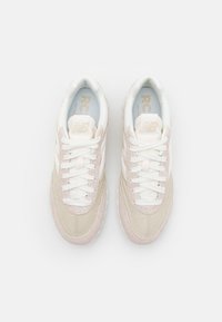 Beige and light pink sneakers with a suede and leather upper, white laces, and a textured sole. Interior features blue branding.